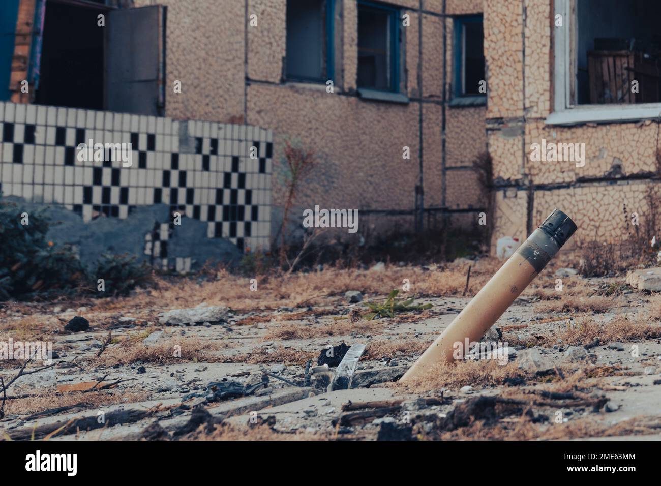 War in Ukraine. Russian invasion of Ukraine. An unexploded rocket projectile sticks into the ground next to a destroyed house Stock Photo