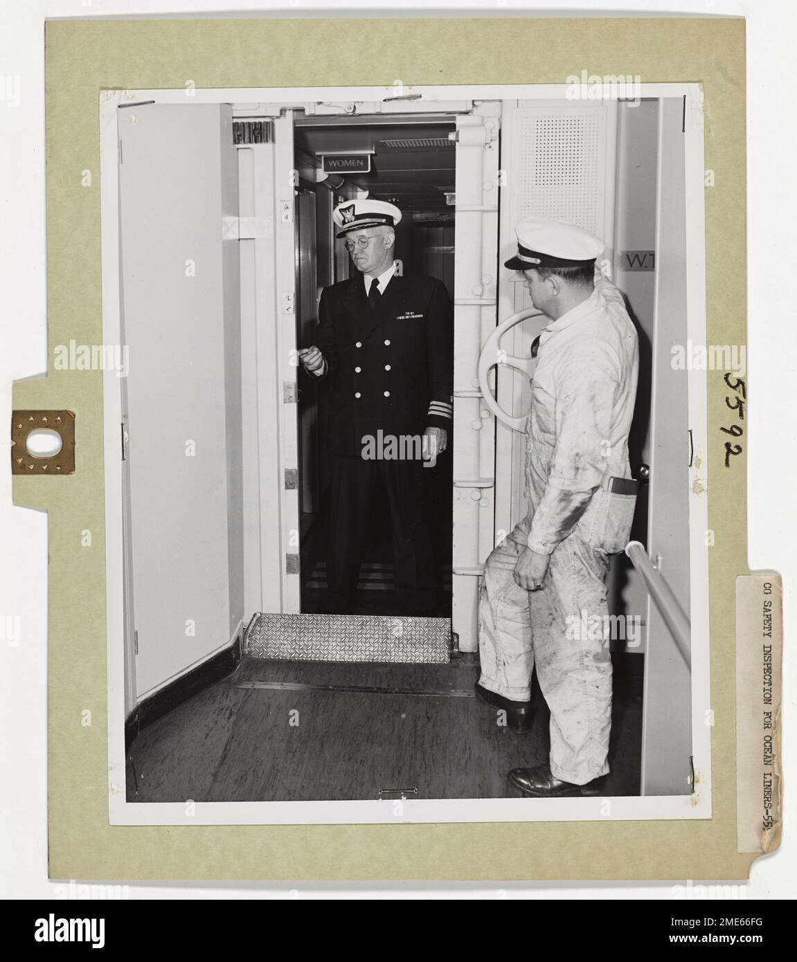 Coast Guard Safety Inspections for Ocean Liners. Commander Paul H. Brown (left), USCG, joins Lieutenant (jg) Frederick O. Wooley below decks to check closure of watertight doors. Here, they seal the door by local control to insure its operation in case of failure of the master control system. As the heavy door slowly meshes closed, a warning alarm sounds in the passageway. The door, which limits flooding to a small controllable area, closes with sufficient force to cut off a stream of flooding mater or cut through debris that might jam in the doorway. Stock Photo