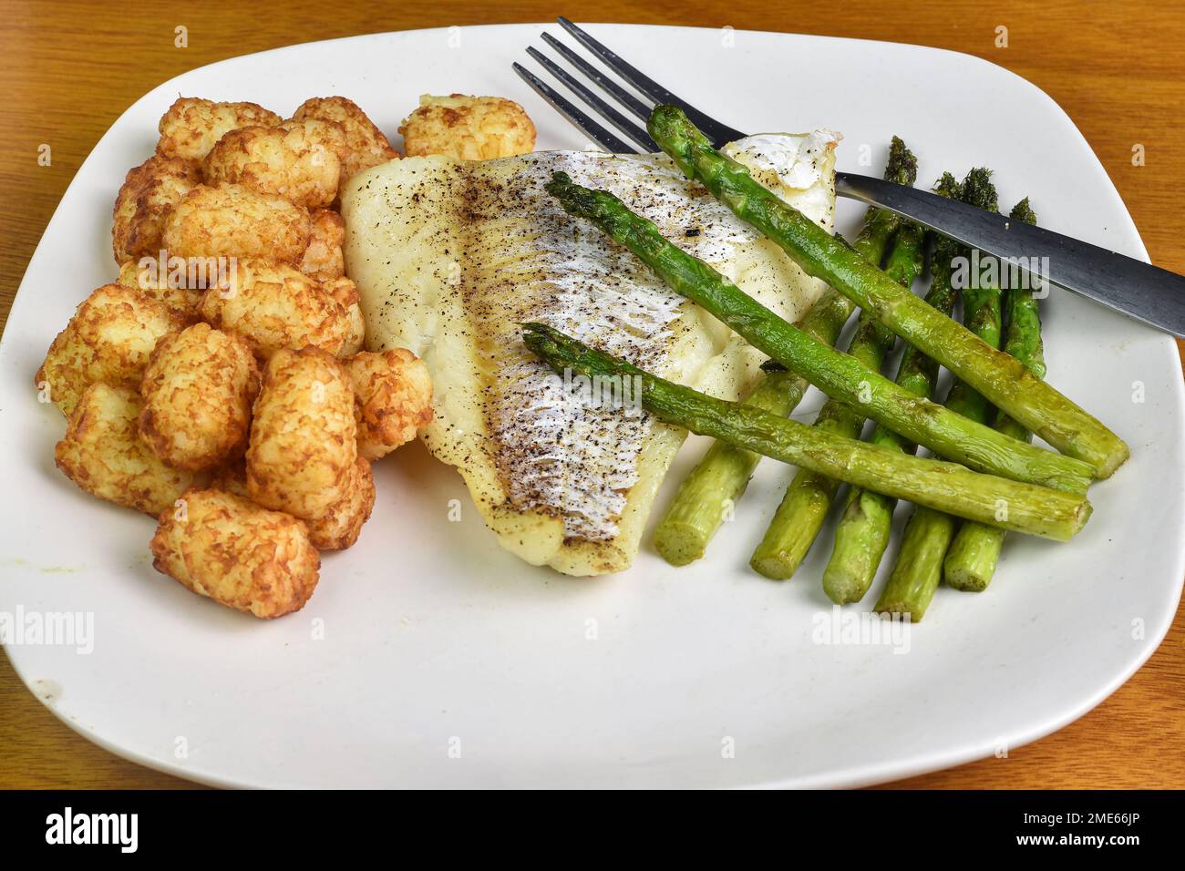 baked season cod served with sauteed asparagus and tater tots Stock ...