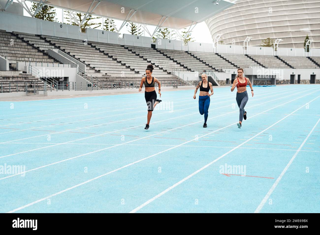 We keep each other on our toes. Full length shot of a young attractive group of athletes racing each other during a track and field workout session. Stock Photo