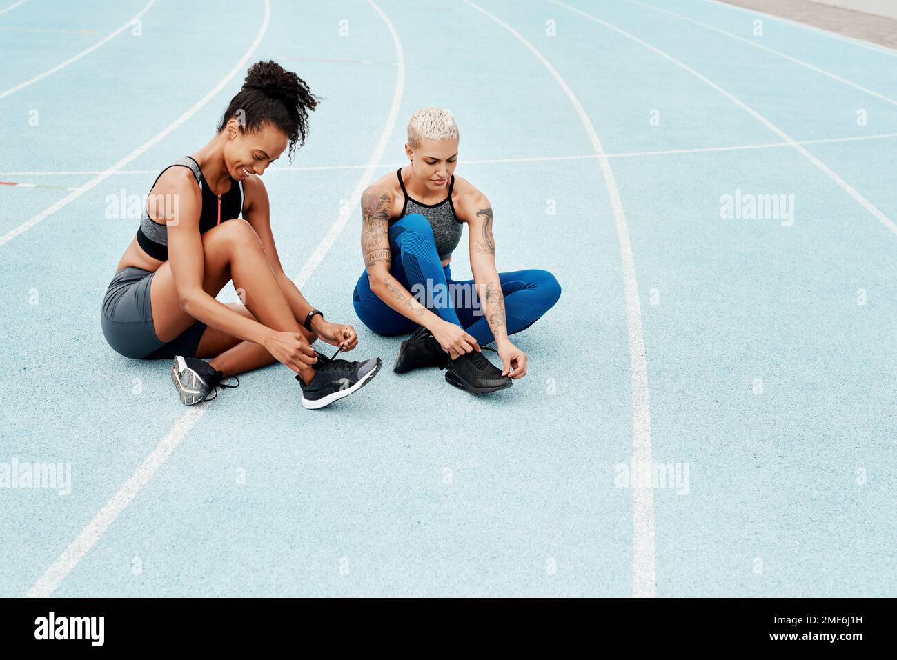 Preparing for your run. Full length shot of two attractive young athletes sitting together and tying their shoelaces before running on a track. Stock Photo