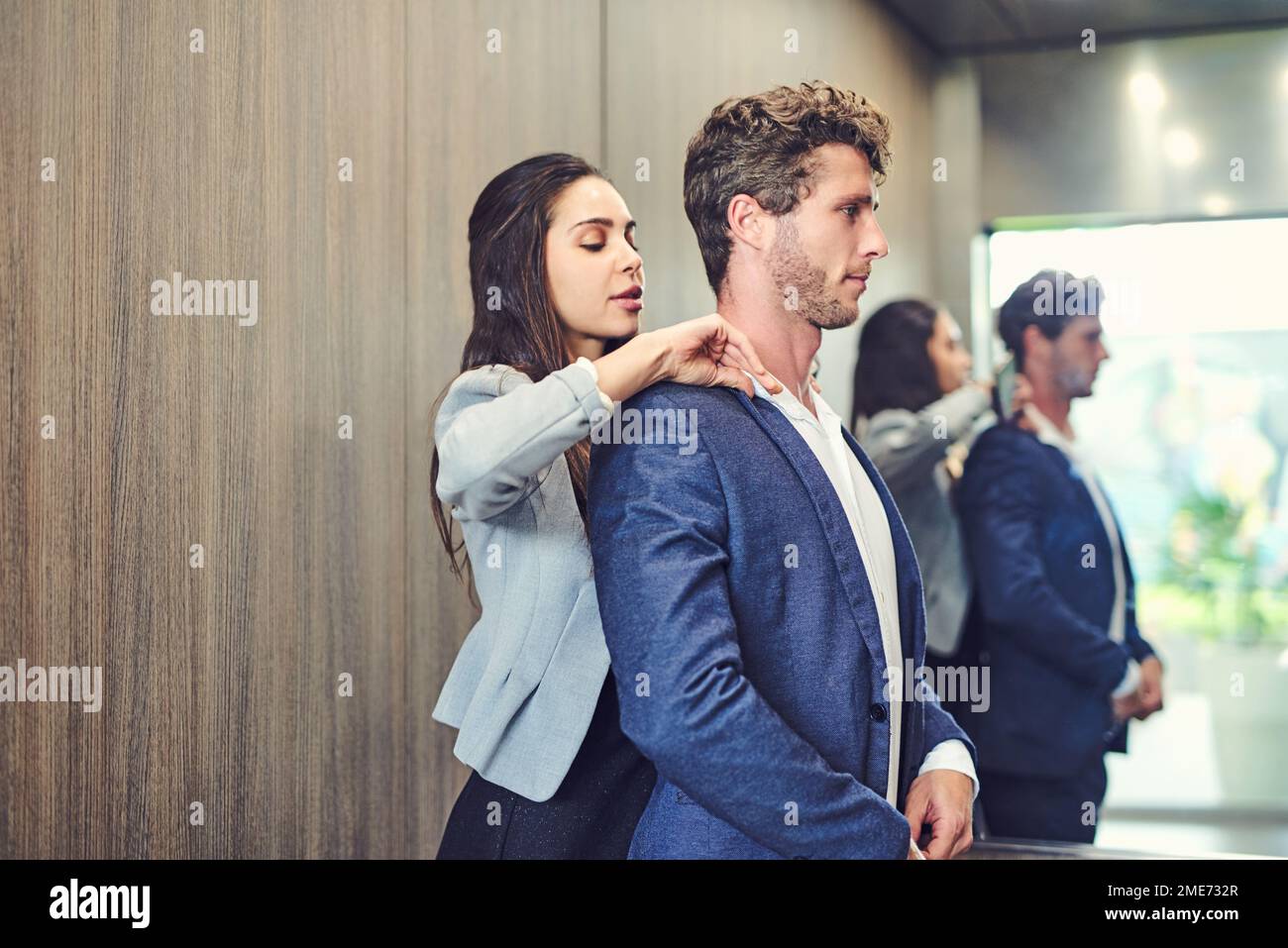 Making sure he looks perfect. a businesswoman adjusting a businessmans collar in an elevator. Stock Photo