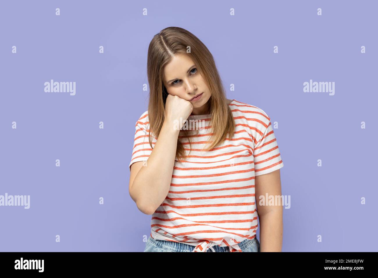 Unhappy depressed blond woman feeling bored with tedious conversation, feels disinterest and apathy, indifferent to life, lack of energy. Indoor studio shot isolated on purple background. Stock Photo