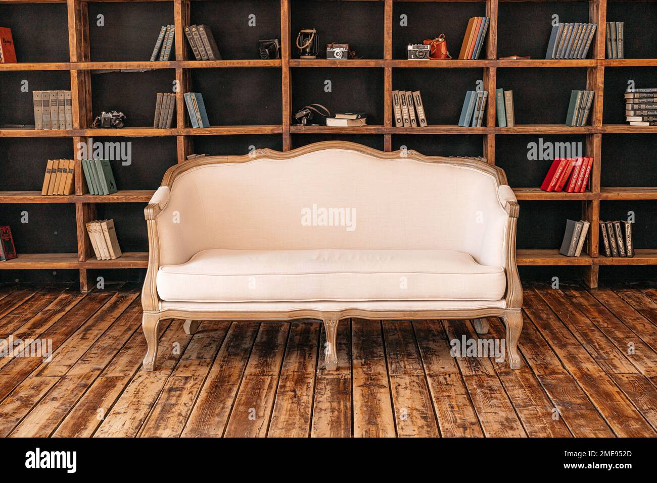 White retro sofa standing in the living room with stylish interior design and collections of books on the bookshelves in the library. Study. Stock Photo