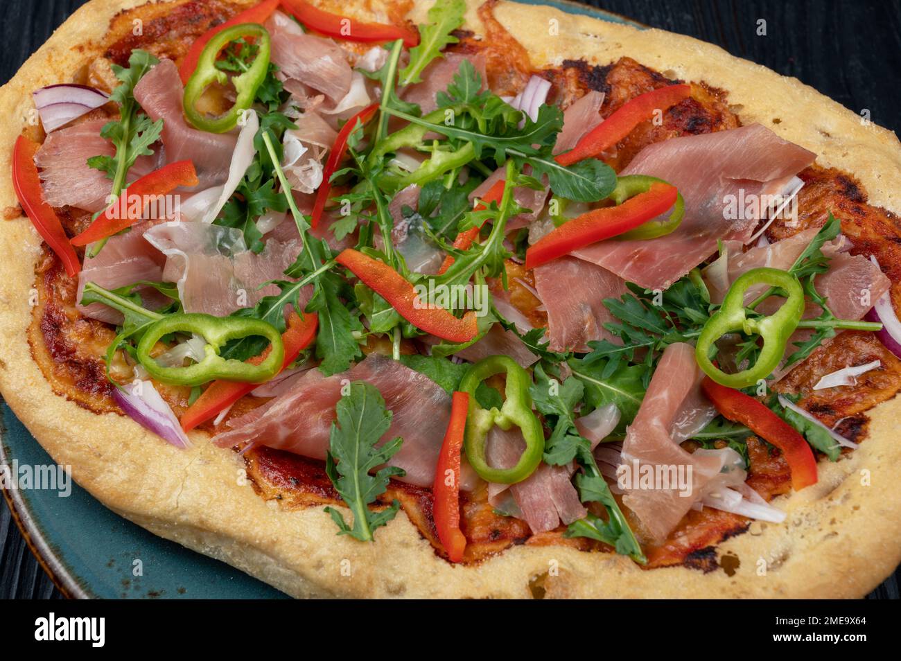Italian Pizza on plate with jamon slices, pepper and fresh arugula leaves on top Stock Photo