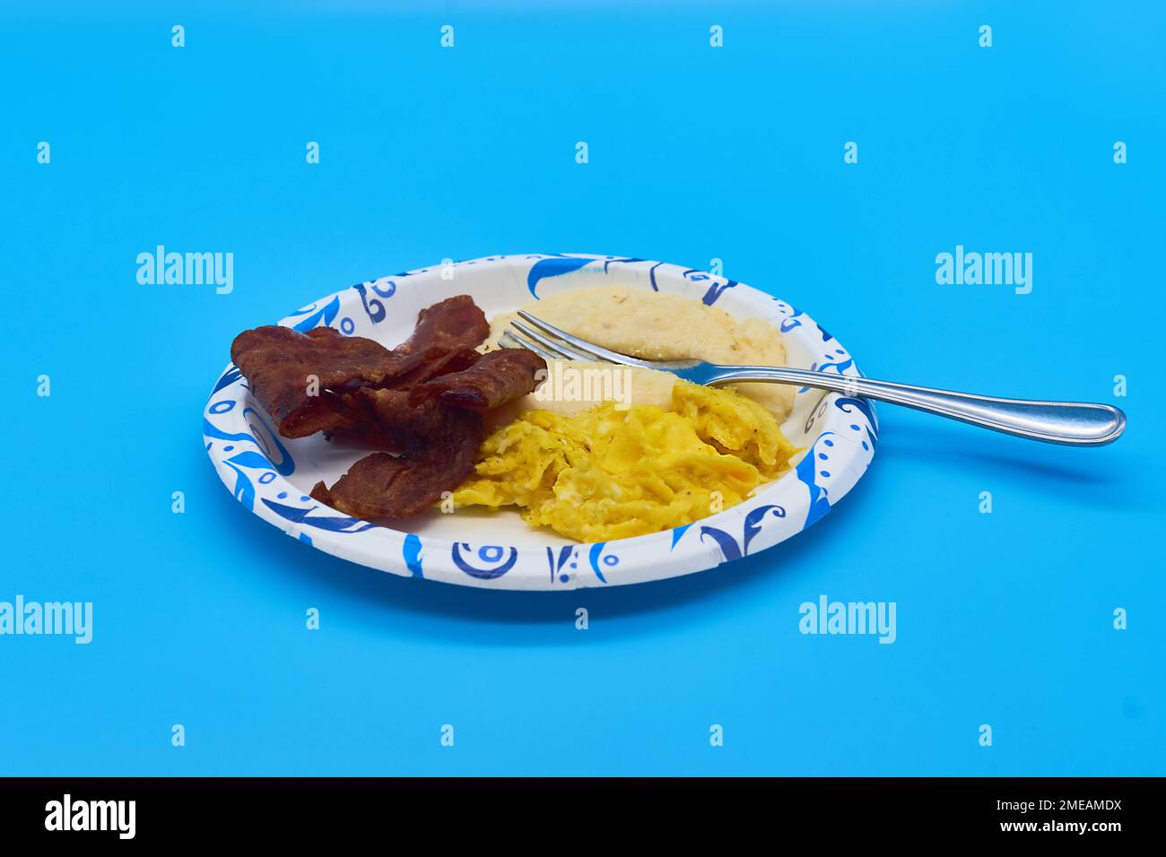 breakfast turkey bacon grits and scrambled eggs on paper plate and light blue background Stock Photo
