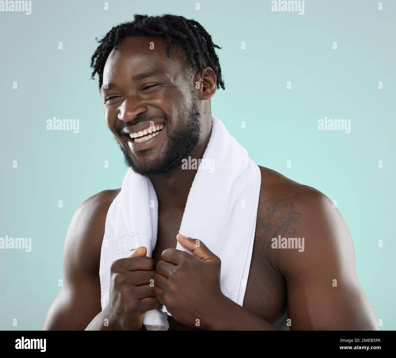 Face, skin and beauty of a man in studio with towel for hygiene and grooming. Healthy and happy black person on blue background for facial glow Stock Photo