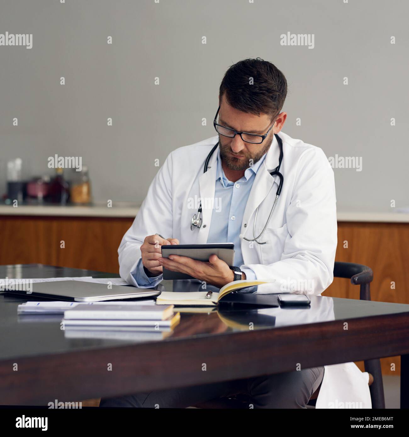 Record-keeping is easy on his digital tablet. a handsome male doctor working on his tablet while sitting in his office. Stock Photo