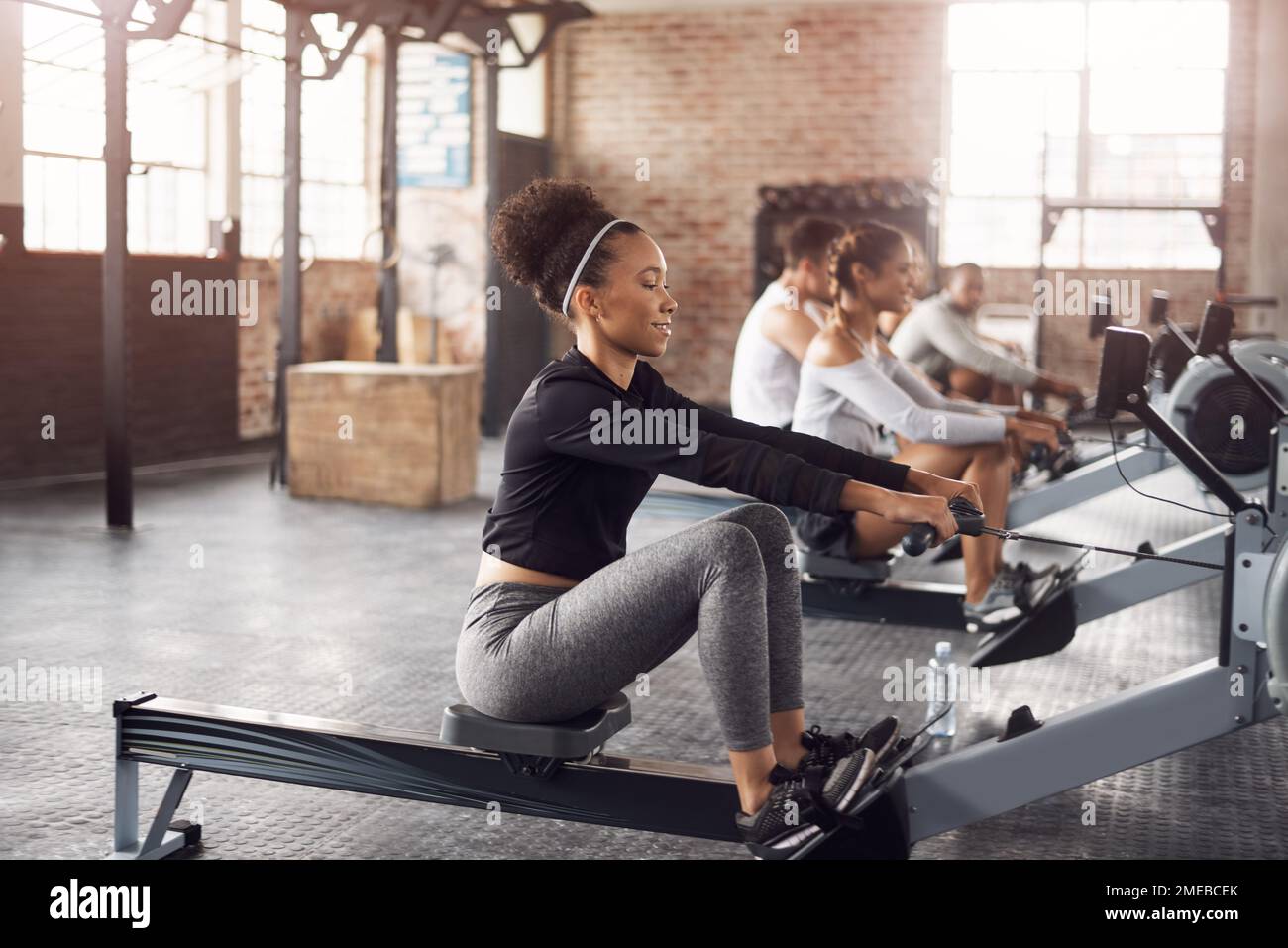 The best way to target every muscle group. a young woman working out with a rowing machine in the gym. Stock Photo