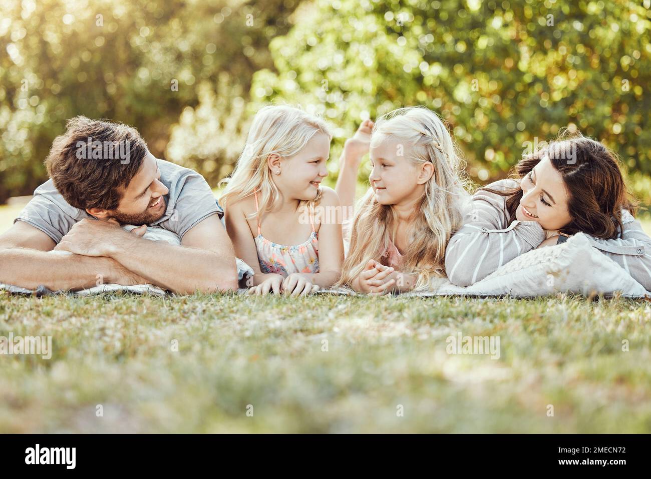 Family, parents and children lying on grass, park and garden in sunshine together. Kids, mom and dad smile on lawn for love, fun and care in nature Stock Photo