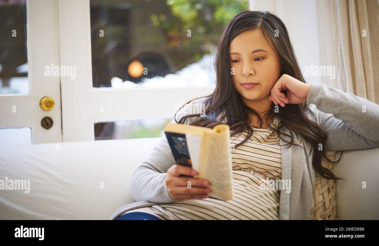 Stuck in a good book. a pregnant woman reading a book at home. Stock Photo