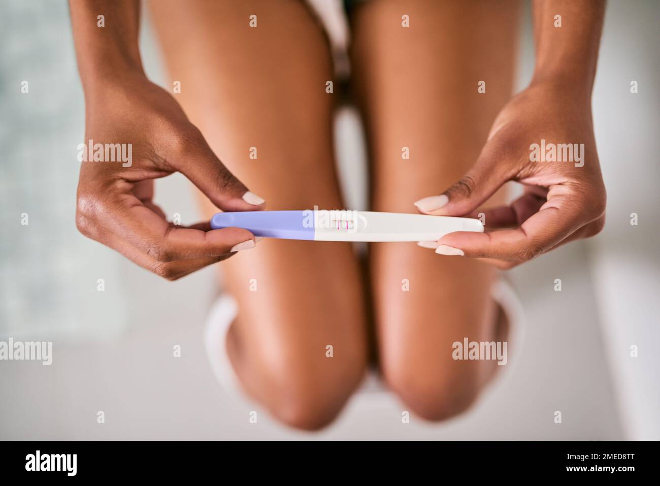 Two little lines changed everything. a woman taking a pregnancy test while sitting on the toilet. Stock Photo