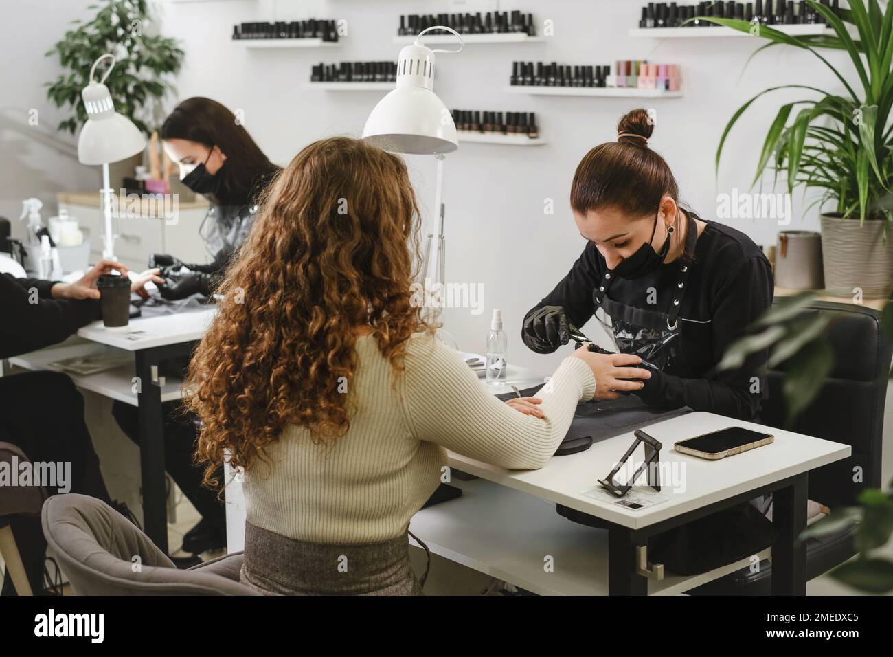 Doing manicure in salon. Female manicurist working on client nails in professional salon. Occupation concept. Customers at beauty green modern studio  Stock Photo