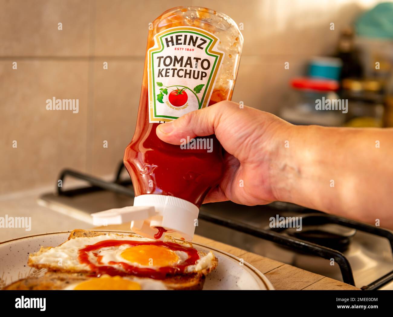 London. UK- 01.22.2023. A person squeezing a bottle of Heinz tomato ketchup on to fried eggs on toast. Stock Photo