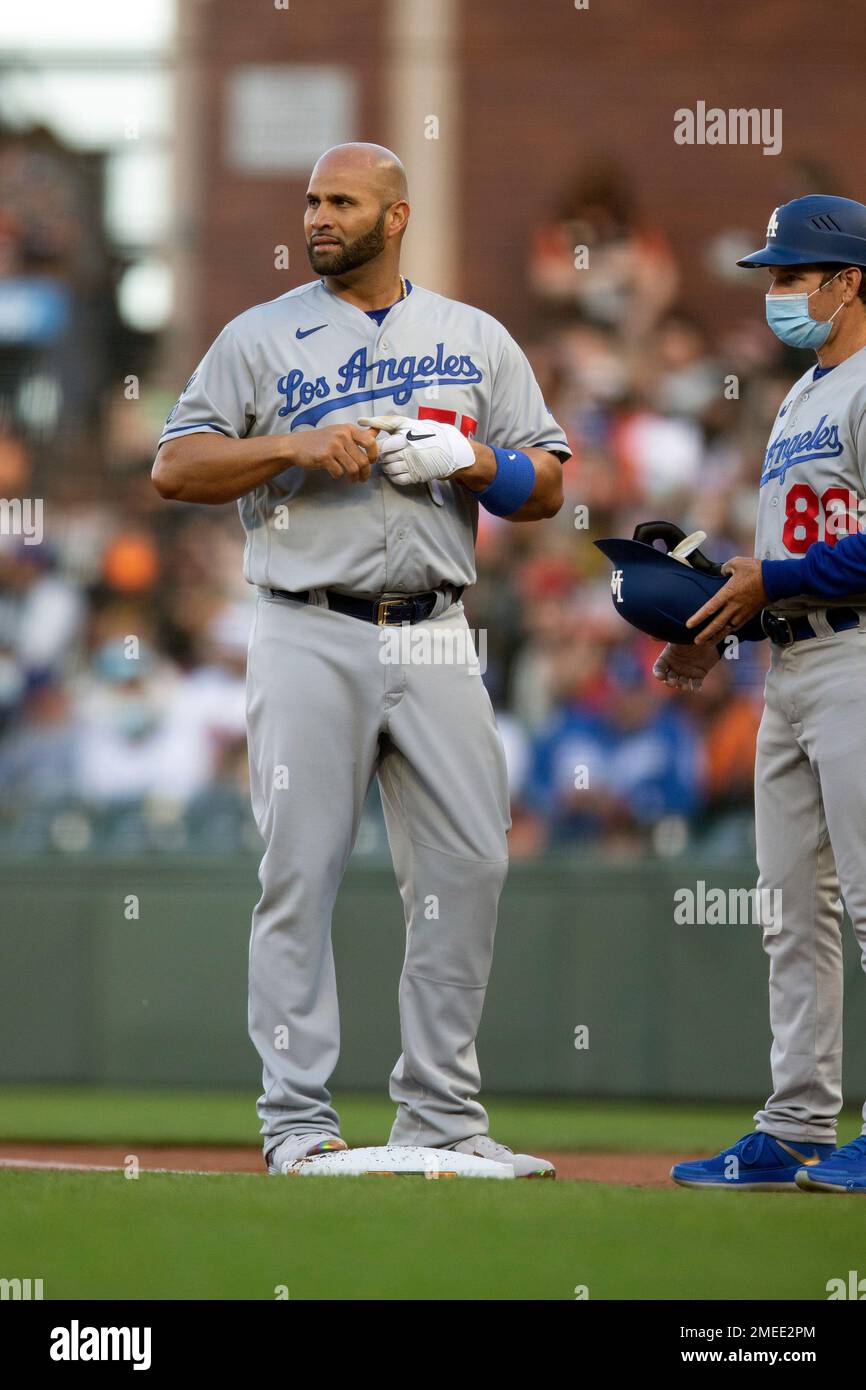 Los Angeles Dodgers' Albert Pujols (55) hands off his batting gear to first  base coach Clayton McCullough (86) after grounding out during the first  inning of a baseball game against the San