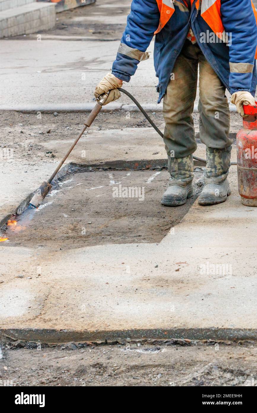 A worker repairs a road by heating a damaged asphalt pavement with a gas burner Stock Photo Alamy
