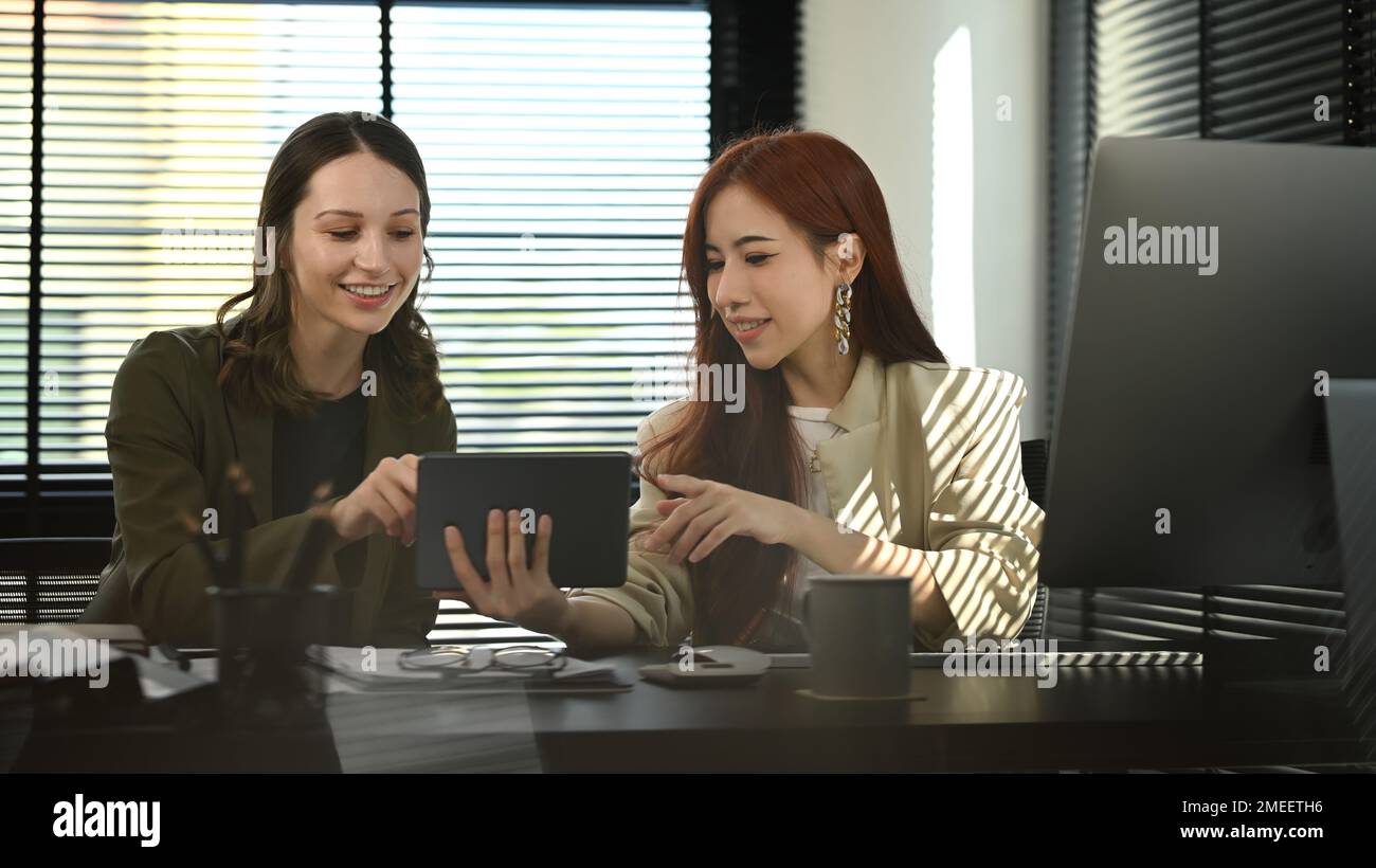 Two stylish businesspeople looking at digital tablet, working on investment and marketing projects Stock Photo