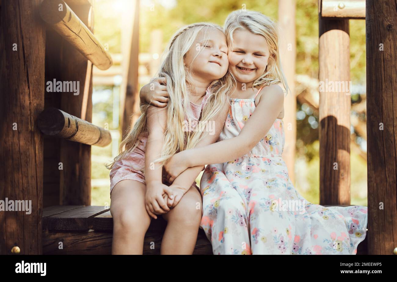 Happy, hug and girl siblings at playground for bonding, wellness and outdoor summer fun together. Care, freedom and happiness of young kids embracing Stock Photo