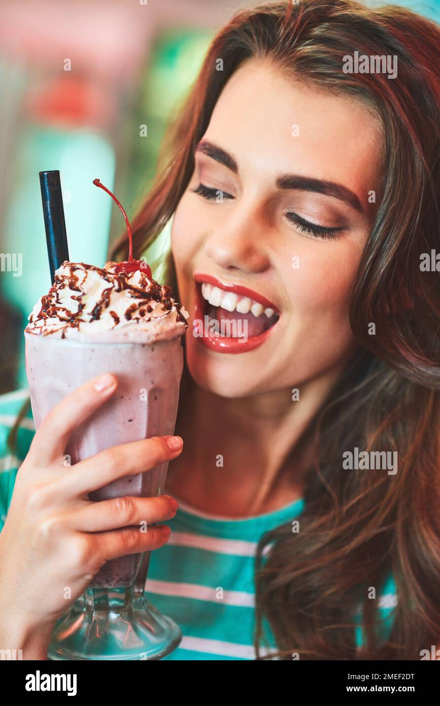 This milkshake is the cherry top to my day. a beautiful young woman drinking a milkshake in a diner. Stock Photo