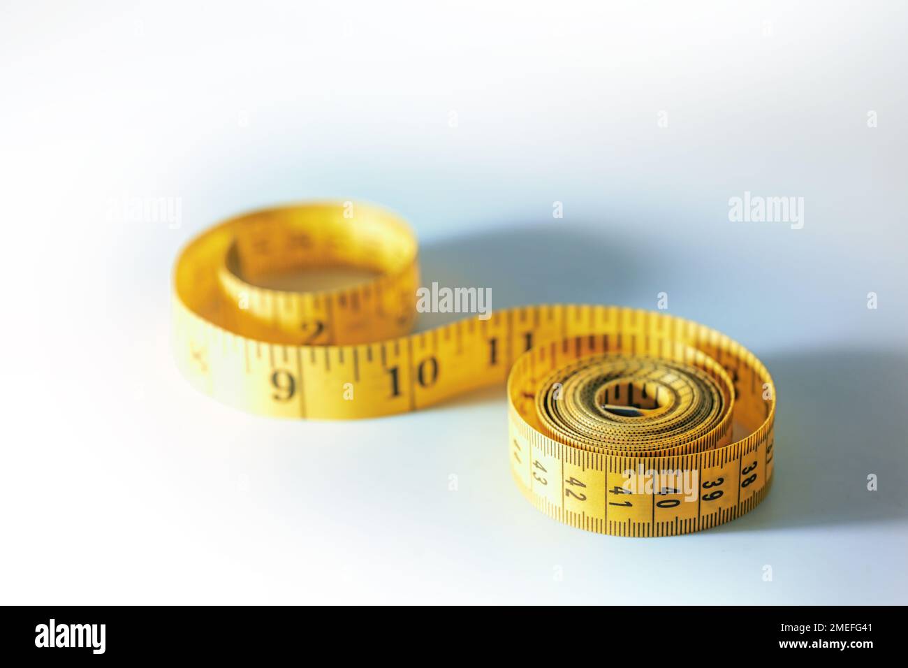 Yellow tape measure rolled up into spirals, sewing tool or symbol for slimming diet, light gray blue background with copy space, selected focus, narro Stock Photo