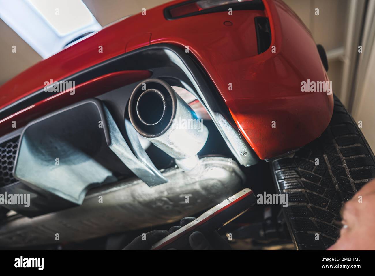 A close shot of a exhaust pipe and a red car's rear, Repair shop concept. High quality photo