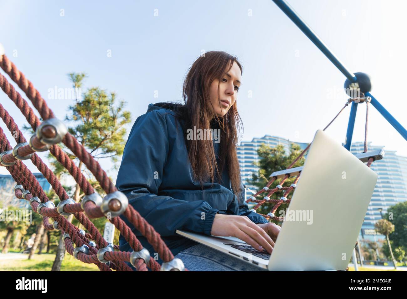Portrait of young beautiful freelancer woman sitting in hammock in park and working at laptop. Stock Photo
