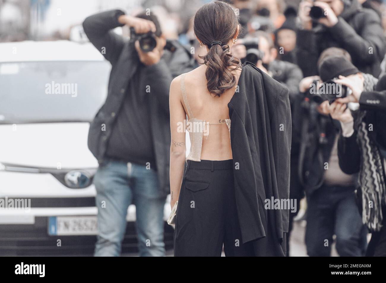 Milan, Italy - February 24, 2022: Back view of female star in top with jacket over shoulder and ponytail standing against paparazzi taking photos Stock Photo