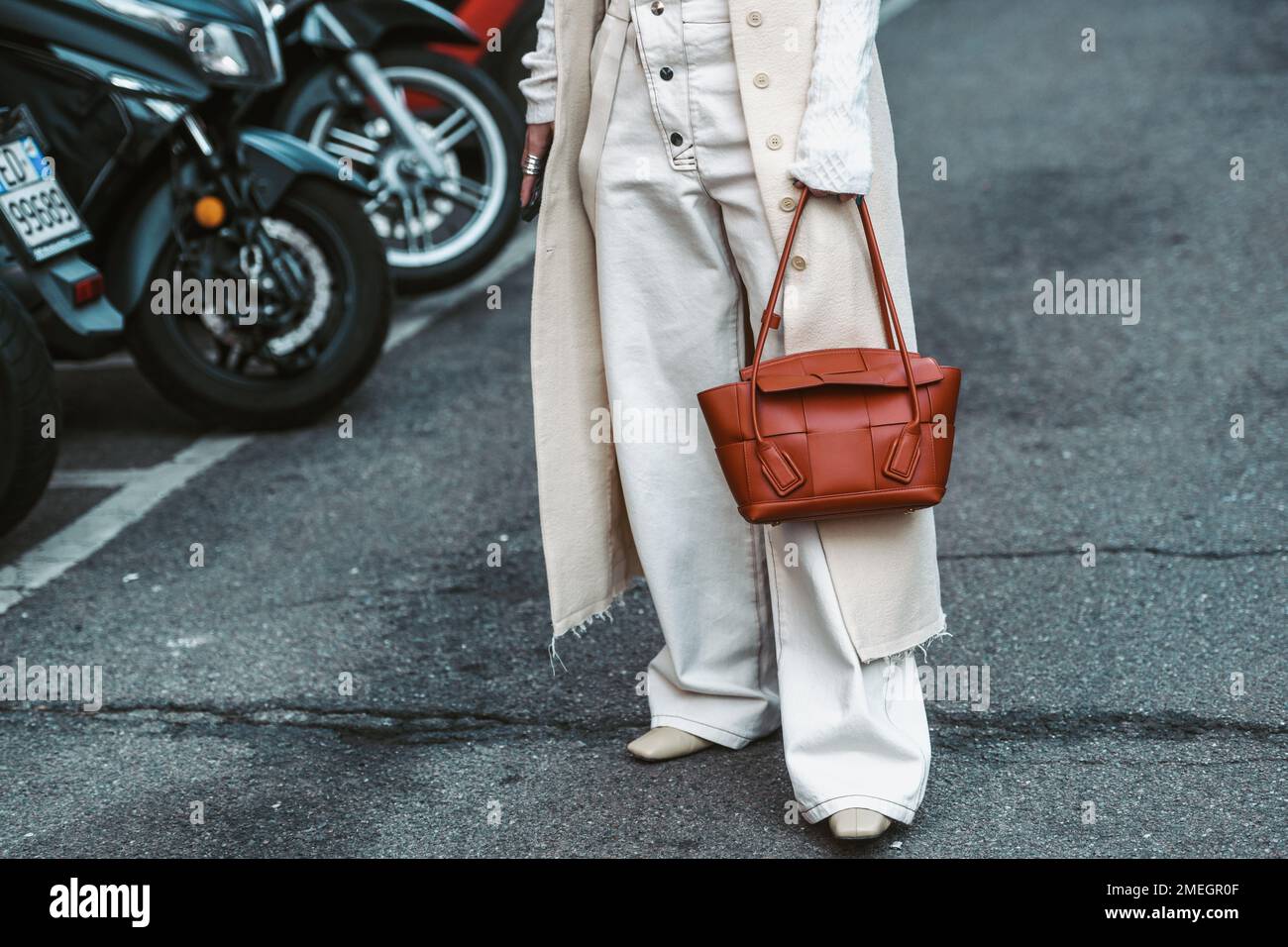 Milan, Italy - February 25, 2022: Woman in white denim and long coat holding brown handbag during Milan Fashion Week Stock Photo