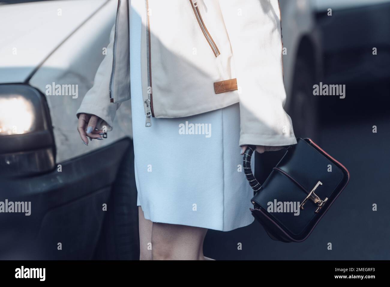 Milan, Italy - February 24, 2022: Crop anonymous stylish female in white short dress beige zip up leather jacket with black handbag. Stock Photo