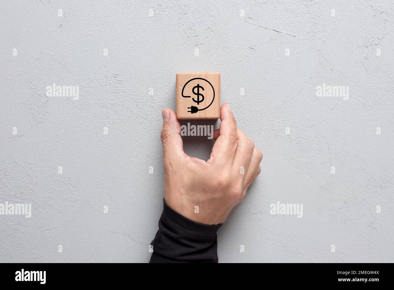 Reducing electricity costs. Energy consumption savings. Male hand puts a cube with energy or electricity cost saving symbol. Stock Photo