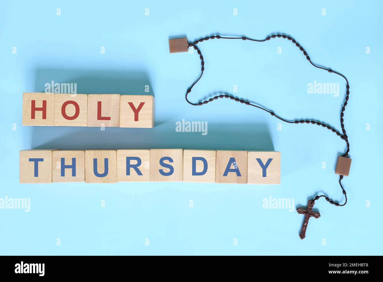 Maundy Thursday holy week concept. Wooden blocks typography with rosary flat lay in blue background. Stock Photo