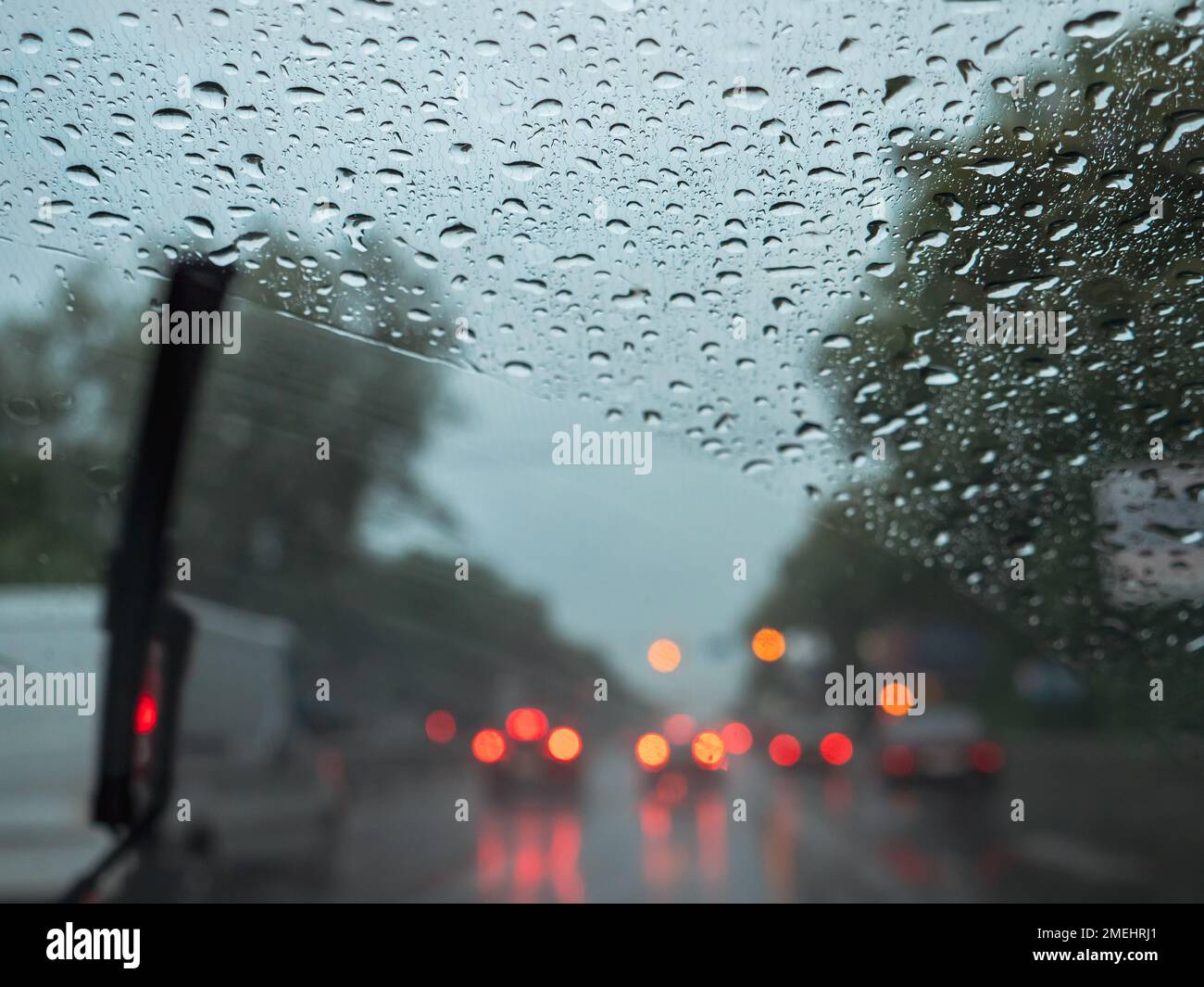 Closeup of raindrops on a windshield, blurry wipers cleaning the glass