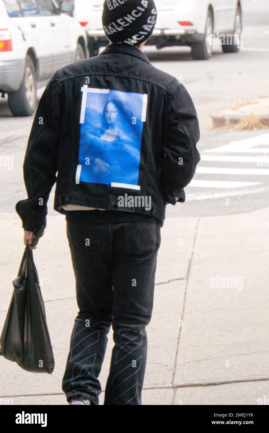 A young man with a replica of the Mona Lisa on the back of his jacket heads off to work. In Flushing, Queens, New York City. Stock Photo