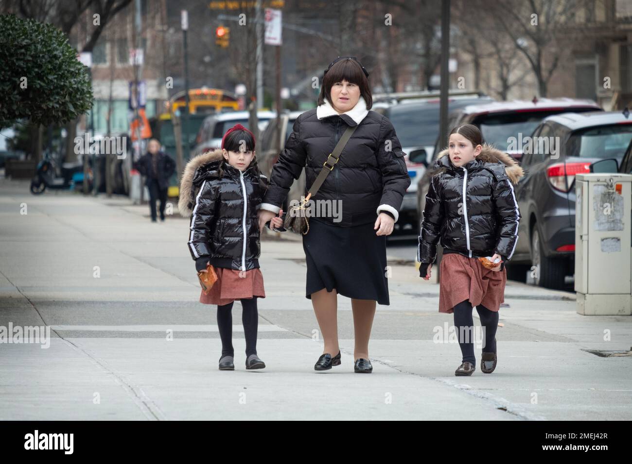 A mother & 2 daughters who are dressed alike, likely because the skirts are from school uniforms. In Brooklyn, New York City. Stock Photo