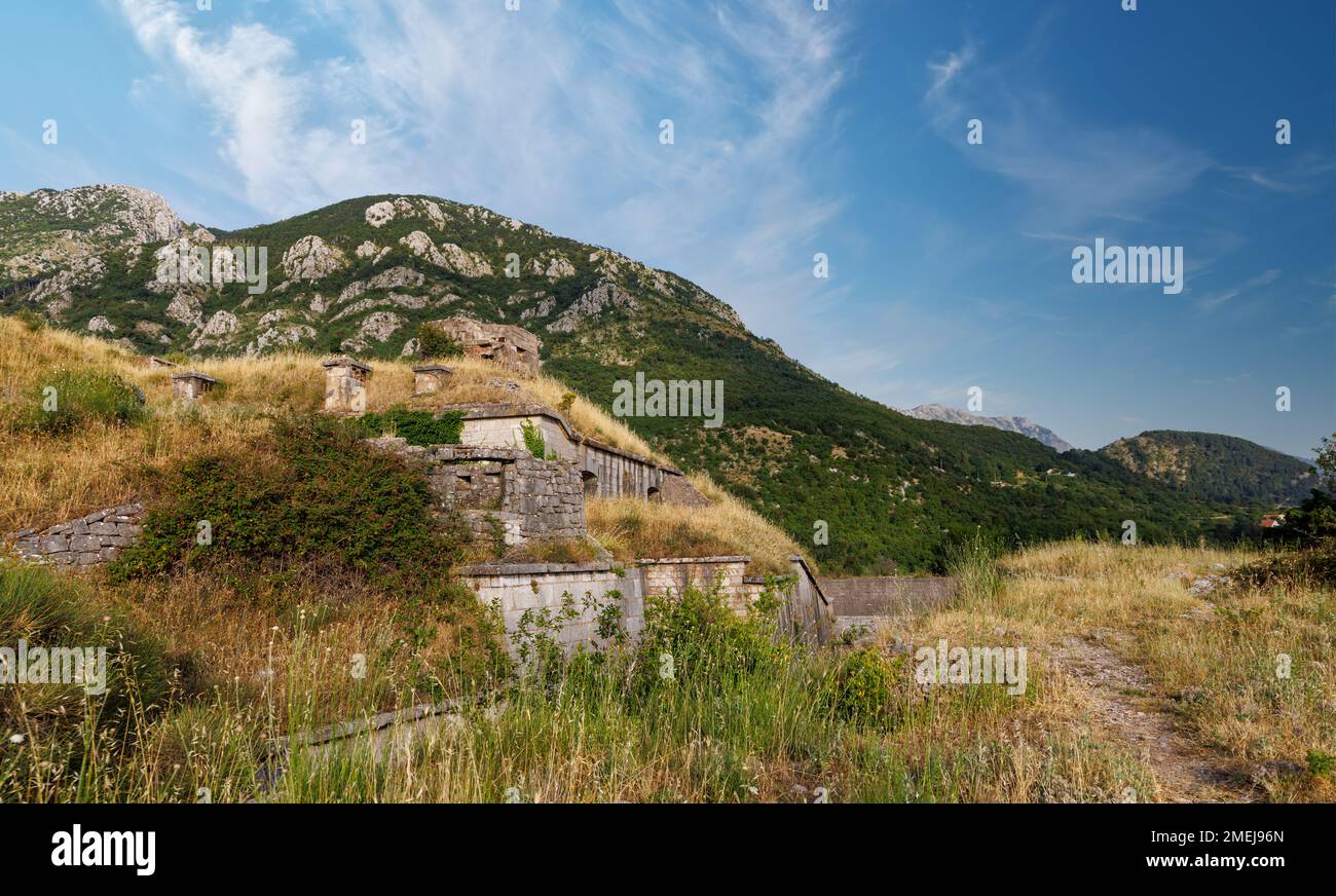 Historical fortress on top of the Montenegrin mountains against the backdrop of coastal resort tourist towns and a cloudy blue daytime sky Stock Photo