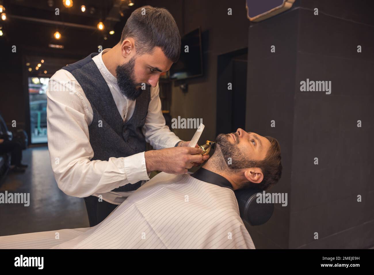 Professional barber carefully trimming the clients beard Stock Photo