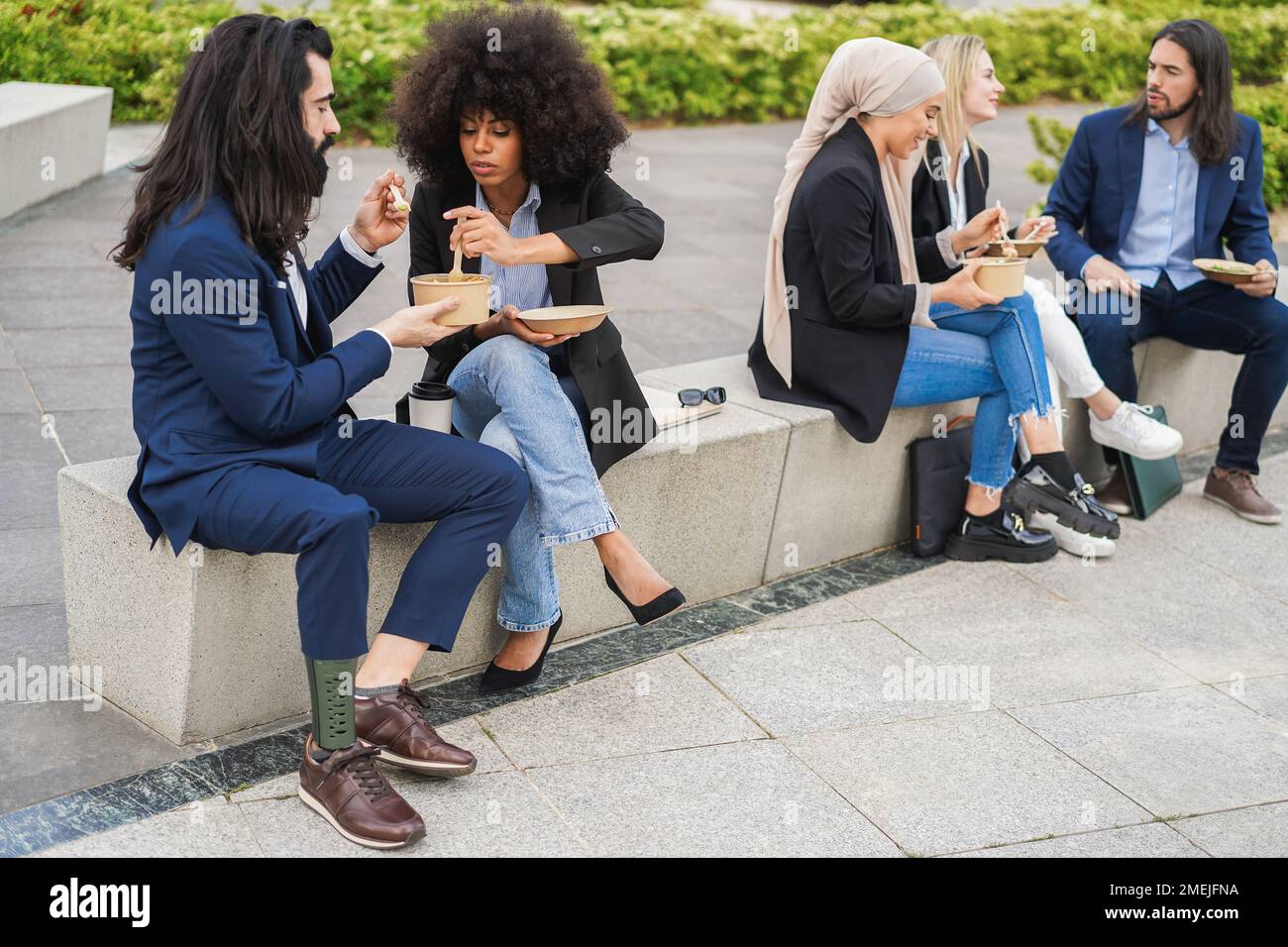 Diverse business people doing lunch break outdoor from office building - Focus on african woman, hand holding plate Stock Photo