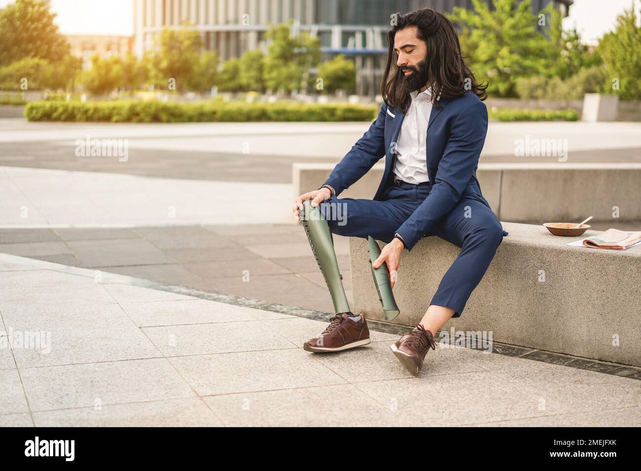 Business man adjusting his prosthetic leg outdoor from office building - Focus on right hand Stock Photo