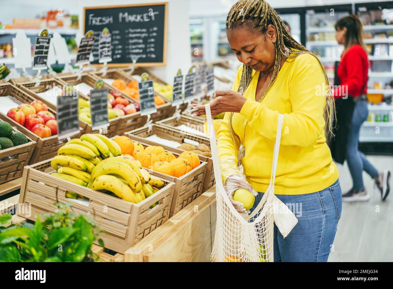 African female customer buying organic food fruits inside eco fresh market - Focus on box of oranges Stock Photo