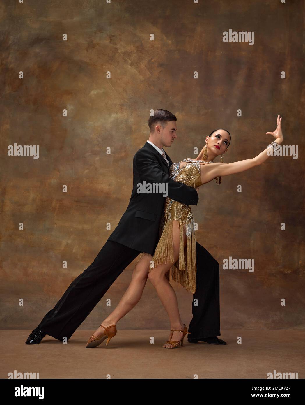 Young man and woman, professional tango dancers in stylish, beautiful stage costumes performing over dark vintage background Stock Photo
