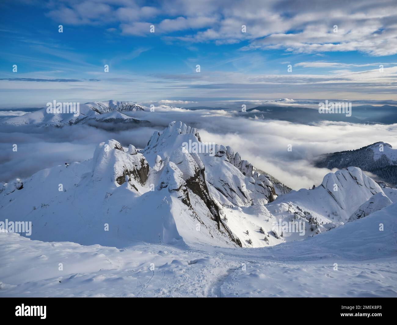 Aerial view of distant mountain peaks above clouds in clear sunny blue sky. Stock Photo