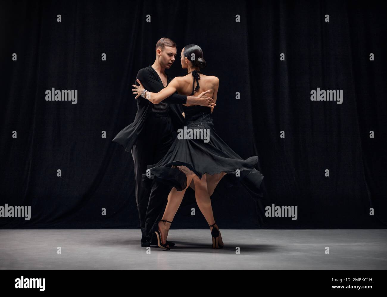 Romantic couple dance. Man and woman, professional tango dancers performing in black stage costumes over black background. Stock Photo