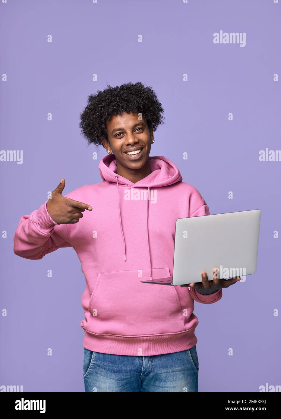 Happy African teen student holding pointing at laptop isolated on purple. Stock Photo