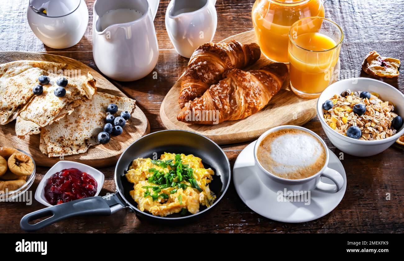 Breakfast served with coffee, orange juice, scrambled eggs, cereals, pancakes and croissants. Stock Photo