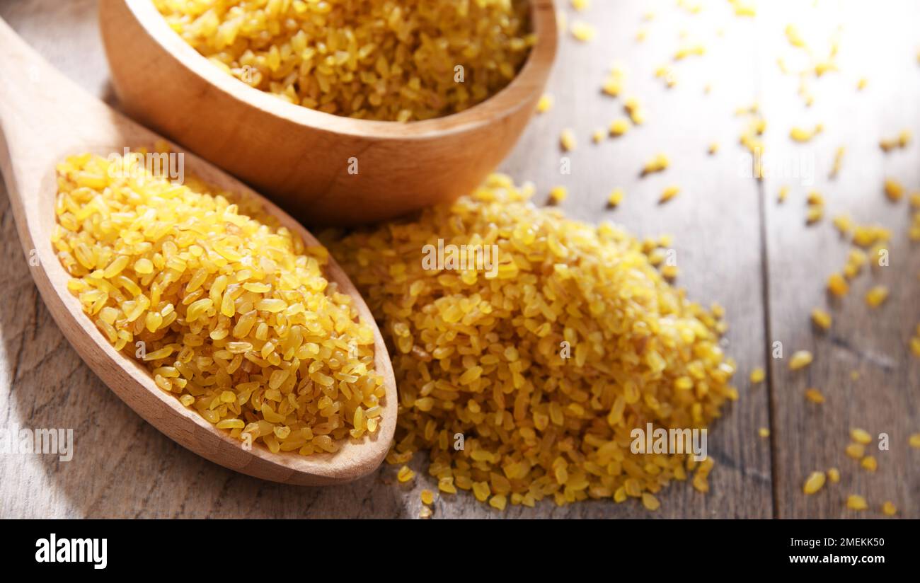 Composition with a bowl and spoon of uncooked bulgur on a table. Stock Photo