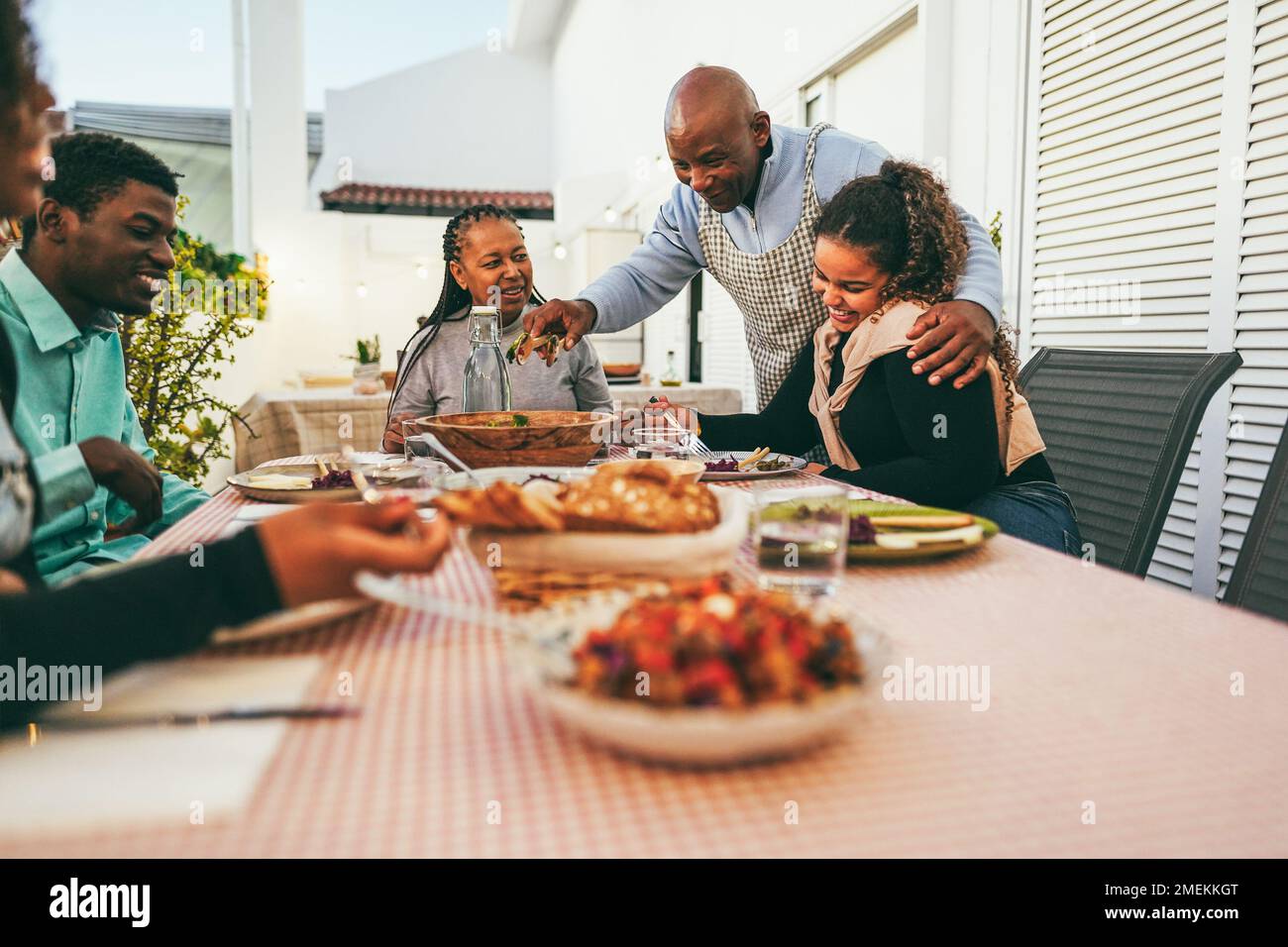 Happy african family eating lunch together at home terrace outdoor - Soft focus on daughter hand Stock Photo