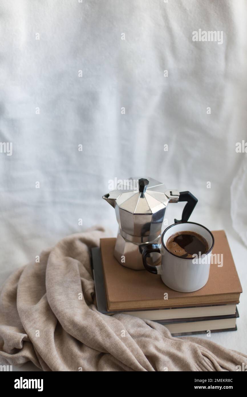 A coffee cup and a moka pot on a few books in a cozy space. Concept of indoor relaxation. Stock Photo