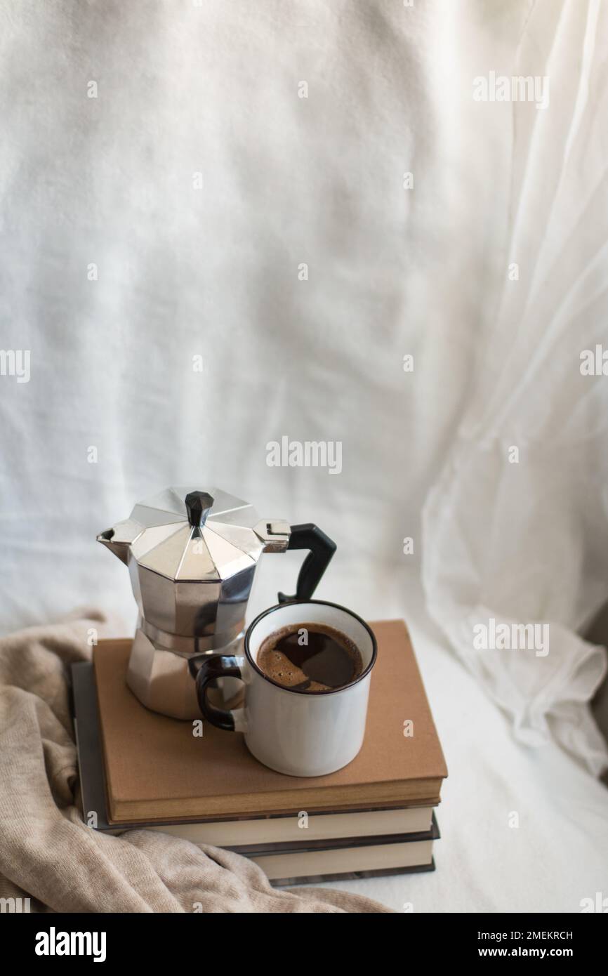 A coffee cup and a moka pot on a few books in a cozy space. Concept of indoor relaxation. Stock Photo