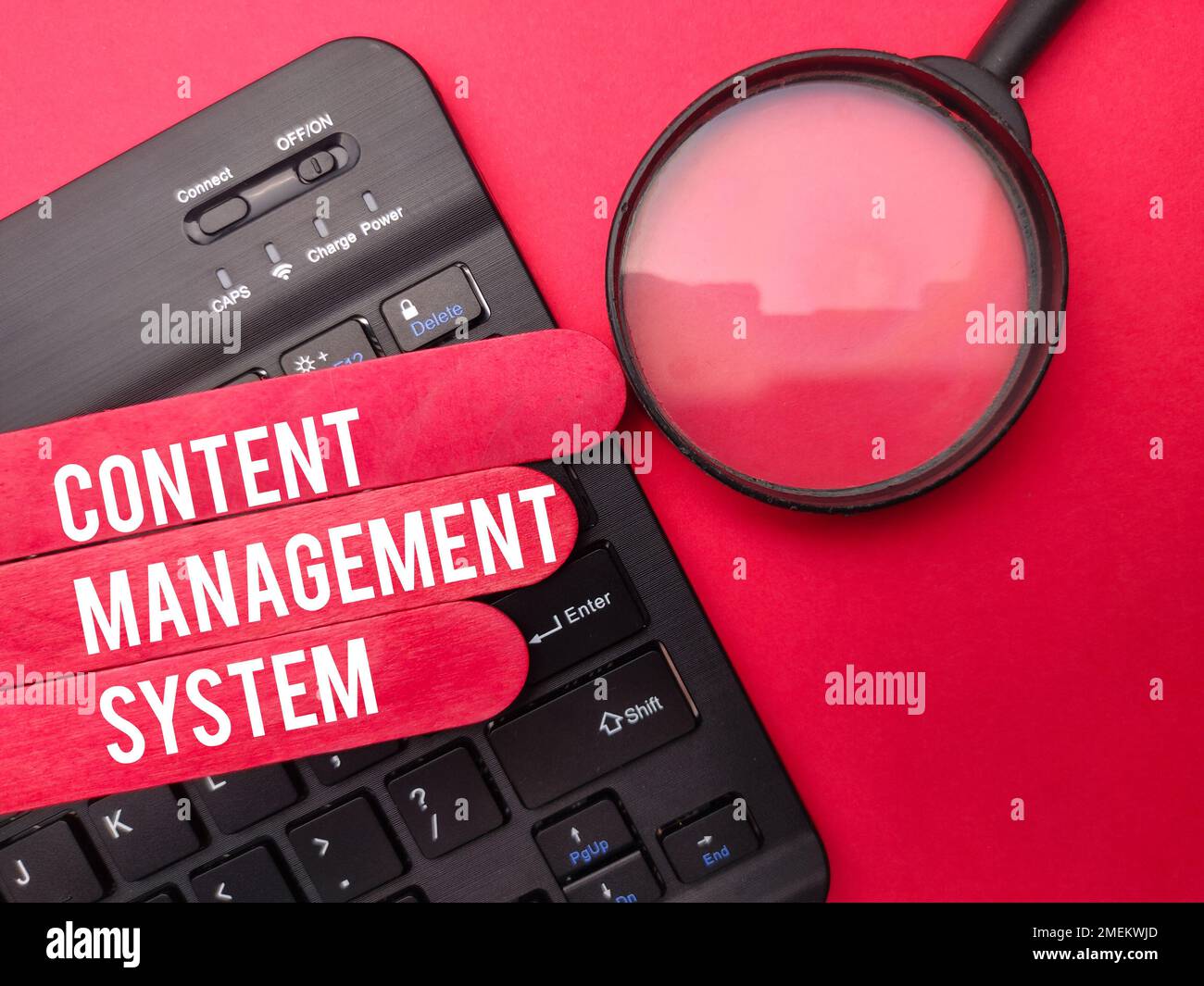 Magnifying glass with the word CONTENT MANAGEMENT SYSTEM on red background. Stock Photo