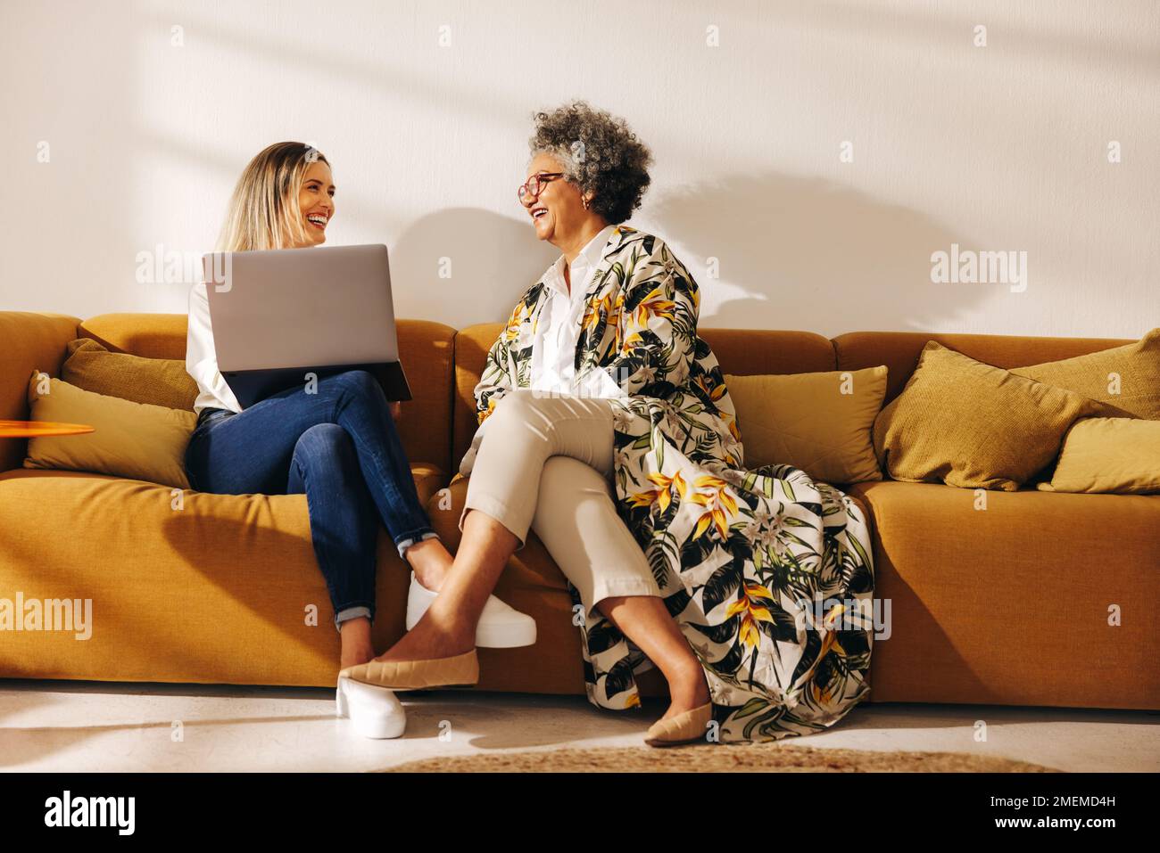 Cheerful businesswomen smiling happily while working together in an office lobby. Successful female entrepreneurs sitting on a couch in a woman-owned Stock Photo